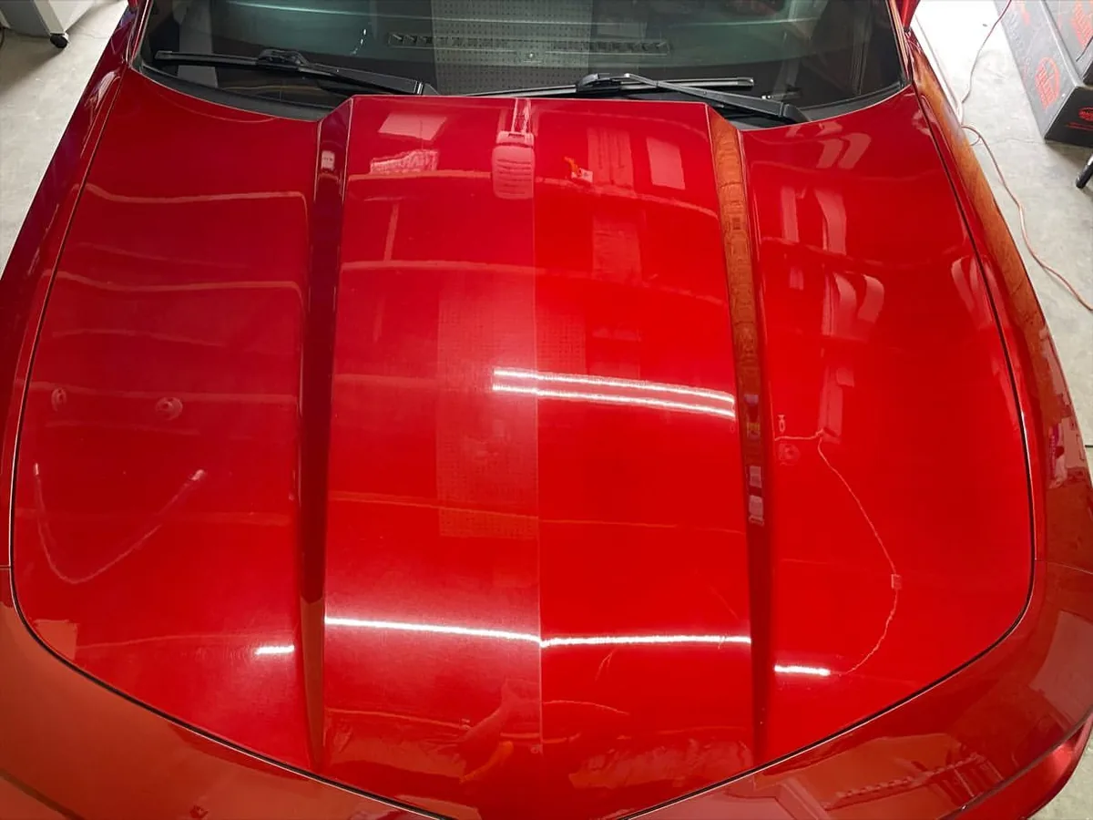 Red Camaro hood showing the difference in paint clarity across a correction test section