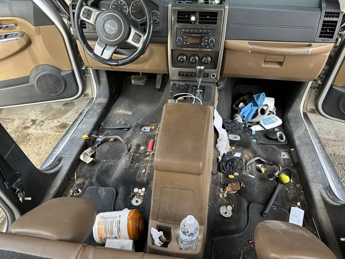 Jeep front interior with seats removed, showing heavy loose debris and buildup before deep cleaning