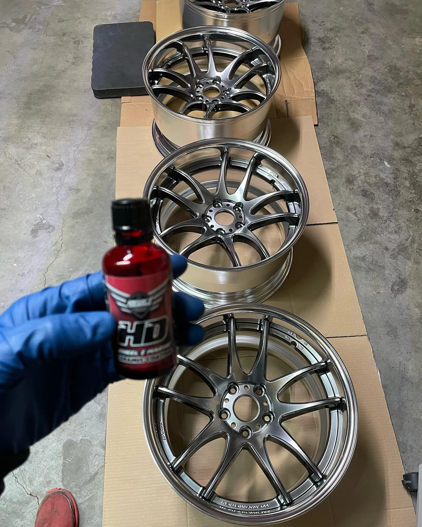 Detailed alloy wheels arranged in a workshop with a finishing product held in the foreground